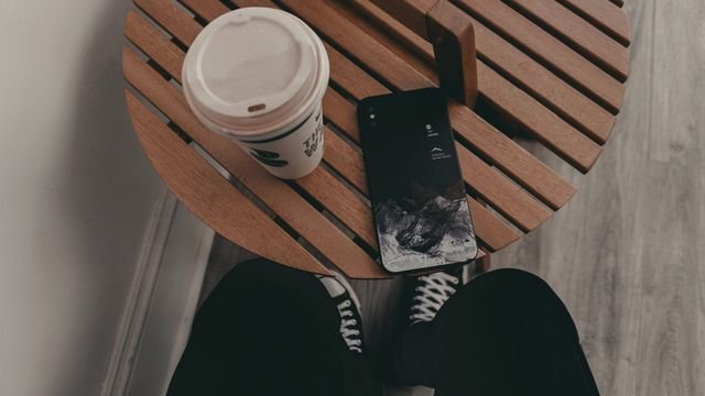 Celular virado para baixo numa mesa de madeira ao lado de um café