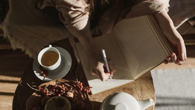 Mãos escrevendo num caderno ao lado de uma xícara de chá