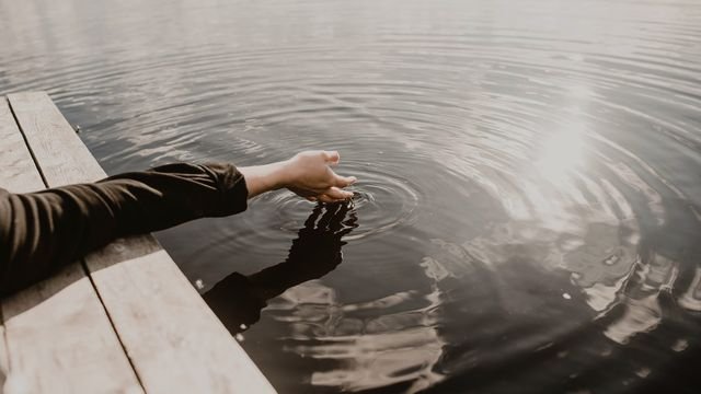 Mão tocando a água calma de um lago a partir de um deque
