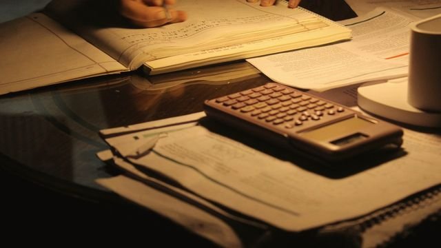 Mesa de estudo à noite com papéis, livros e calculadora sob luz quente